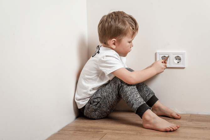 Kid sticking his finger in an outlet, a bad example of electrical safety.