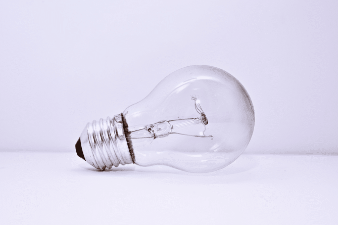 A dead light bulb sitting on a white table with a white wall behind it.