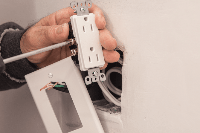 A person working on an outlet while trying to avoid electrical mistakes.