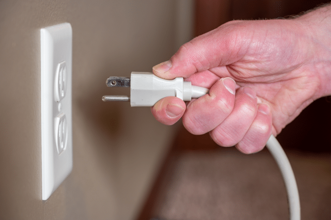 Caucasian hand plugging white cord into a white wall outlet.