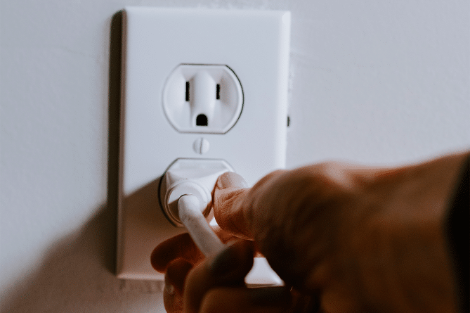 An anonymous person plugging a cord into an electrical socket.