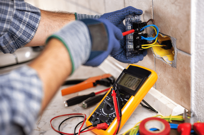 Unknown residential electrician working on an electrical outlet with blue gloves.