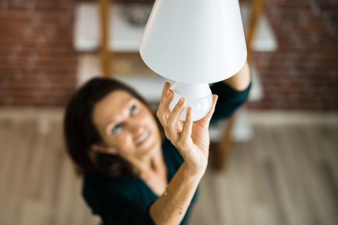 Woman with dark hair changing a light bulb in a ceiling fixture to become LED lighting.