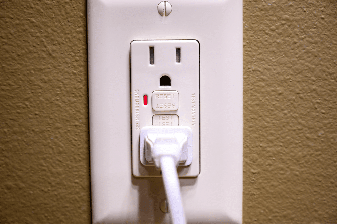 A closeup of a cord plugged into a GFCI outlet on a brown wall.