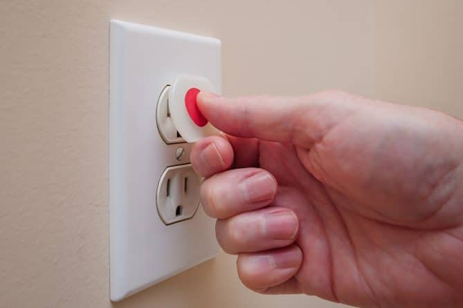 A person putting a cover on their outlet to babyproof their home's electrical system.